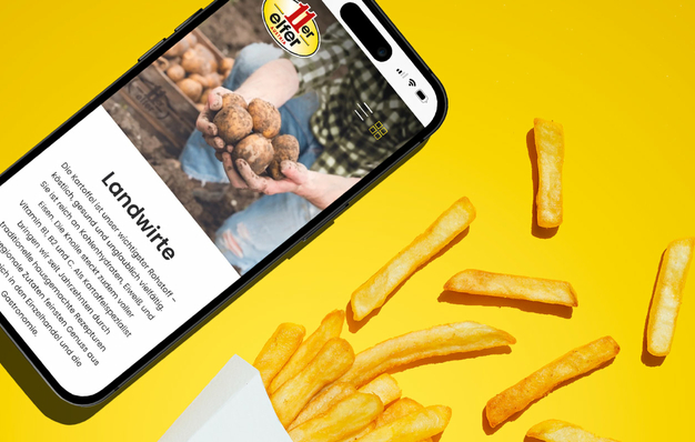 Eine Person, die ein Handy in der Hand hält mit der neuen Website von 11er, im Hintergrund sind Pommes und Burger zu sehen