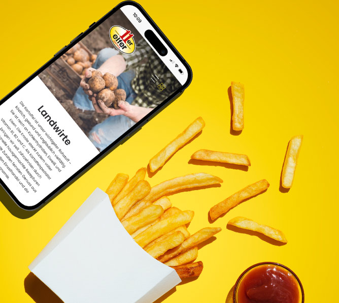 Eine Person, die ein Handy in der Hand hält mit der neuen Website von 11er, im Hintergrund sind Pommes und Burger zu sehen